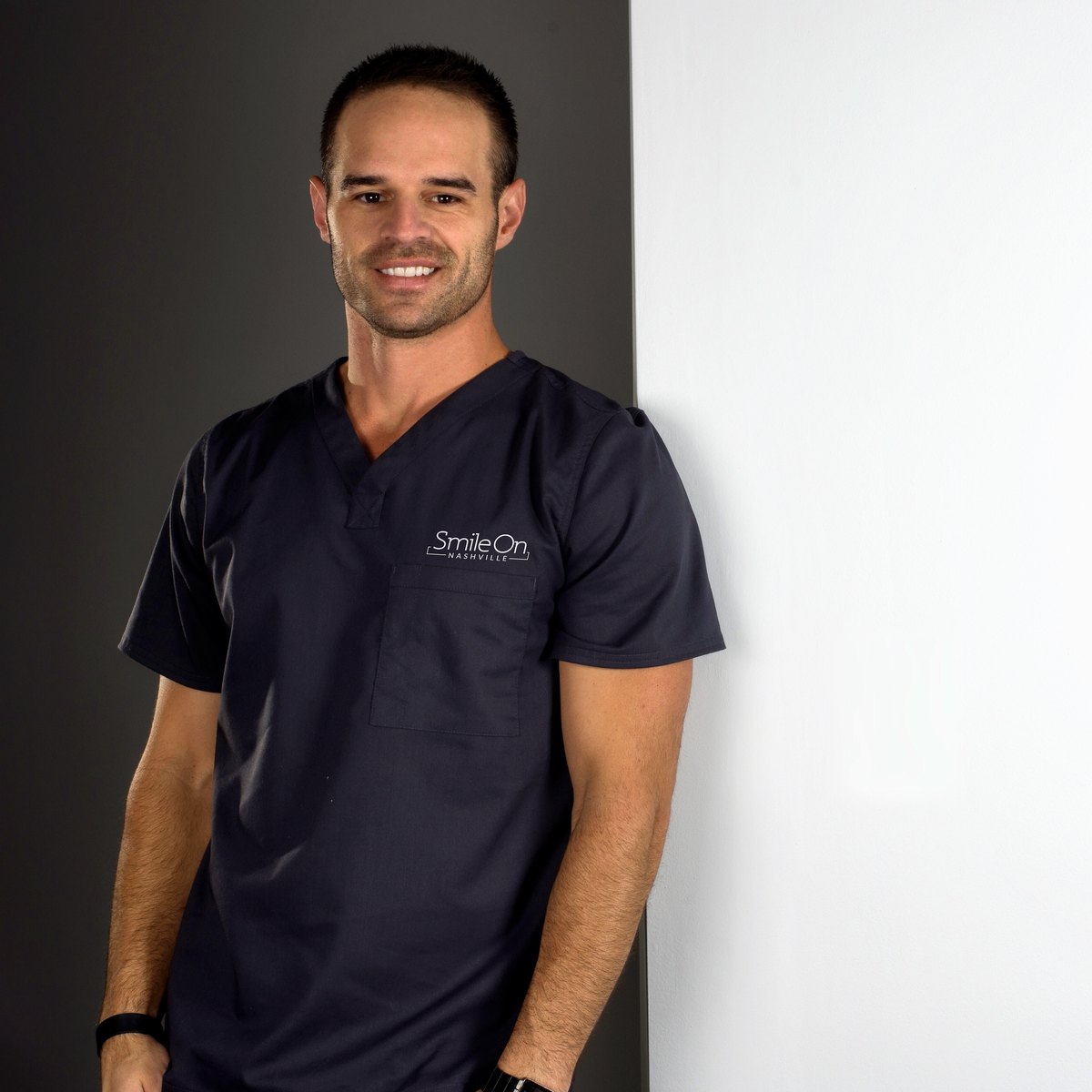 Dr. Jeff Trembley in navy Smile On Nashville scrubs, leaning against the studio wall